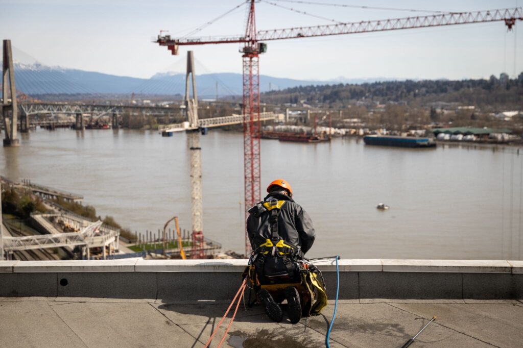 A worker getting ready to go down the side of a building to perform repairs while being anchored to the roof.